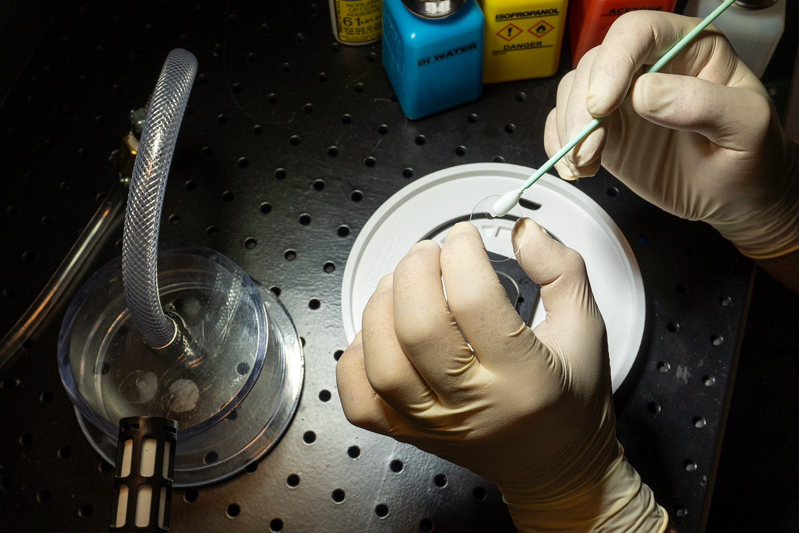 Gloved hands carefully cleaning a precision optical component at Mosaic Optoelectronics